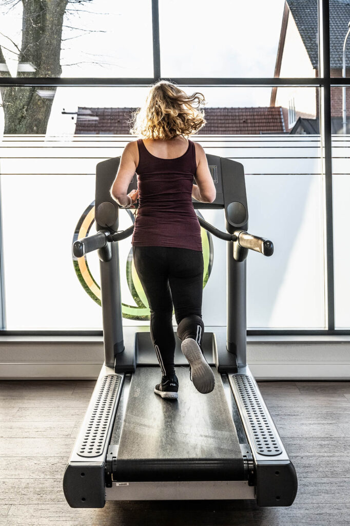 Frau mit blonden Locken auf einem Laufband am joggen, von hinten fotografiert im Sport & Therapiezentrum Schumann