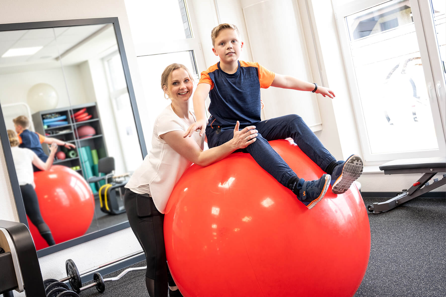 Mitarbeiterin vom Sport & Therapiezentrum Schumann während einer Bobath-Therapie mit einem Jungen auf einem riesigen, roten Gymnastikball