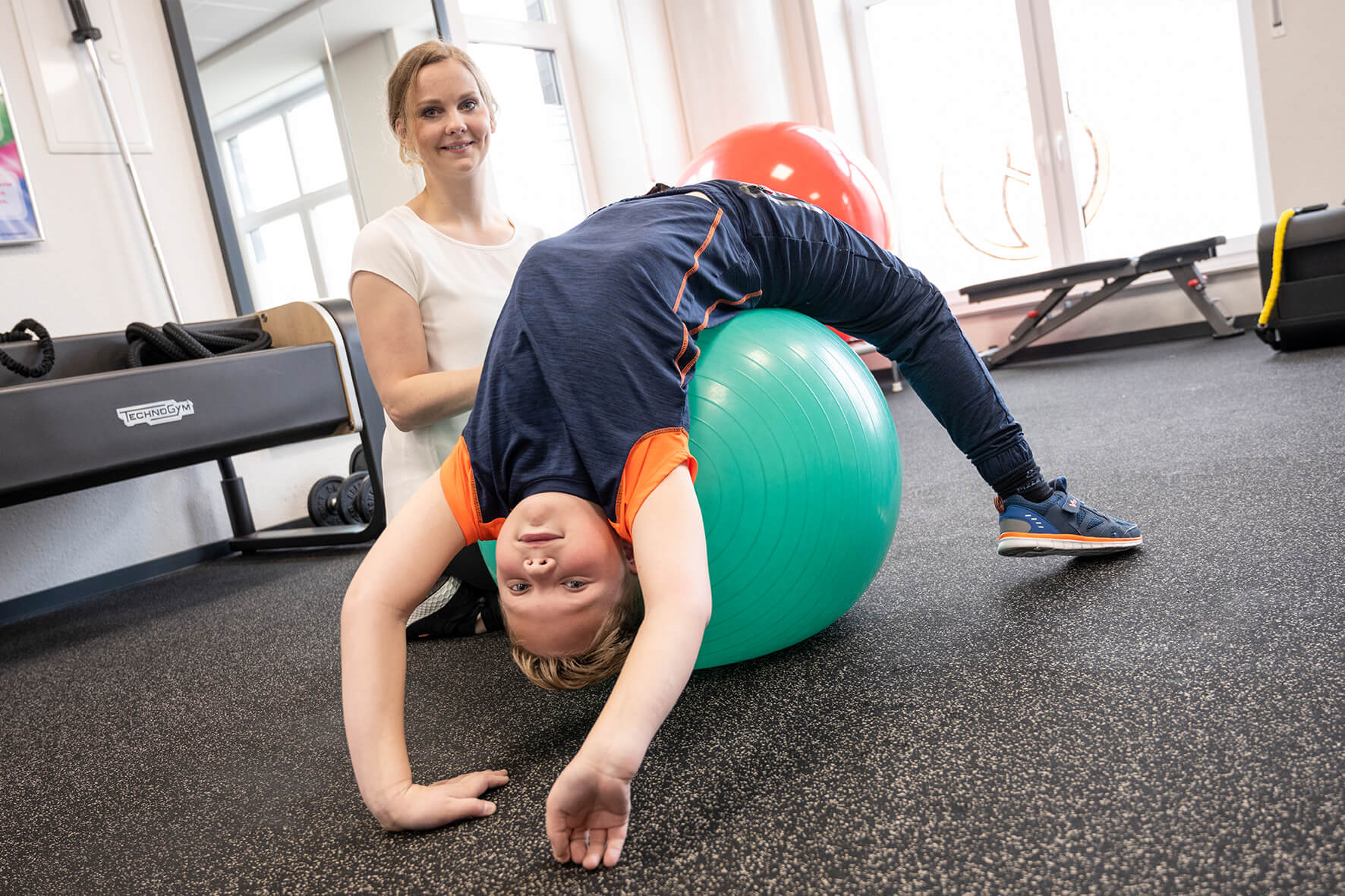 Mitarbeiterin vom Sport & Therapiezentrum Schumann während einer Bobath-Therapie mit einem Jungen auf einem grünen Gymnastikball