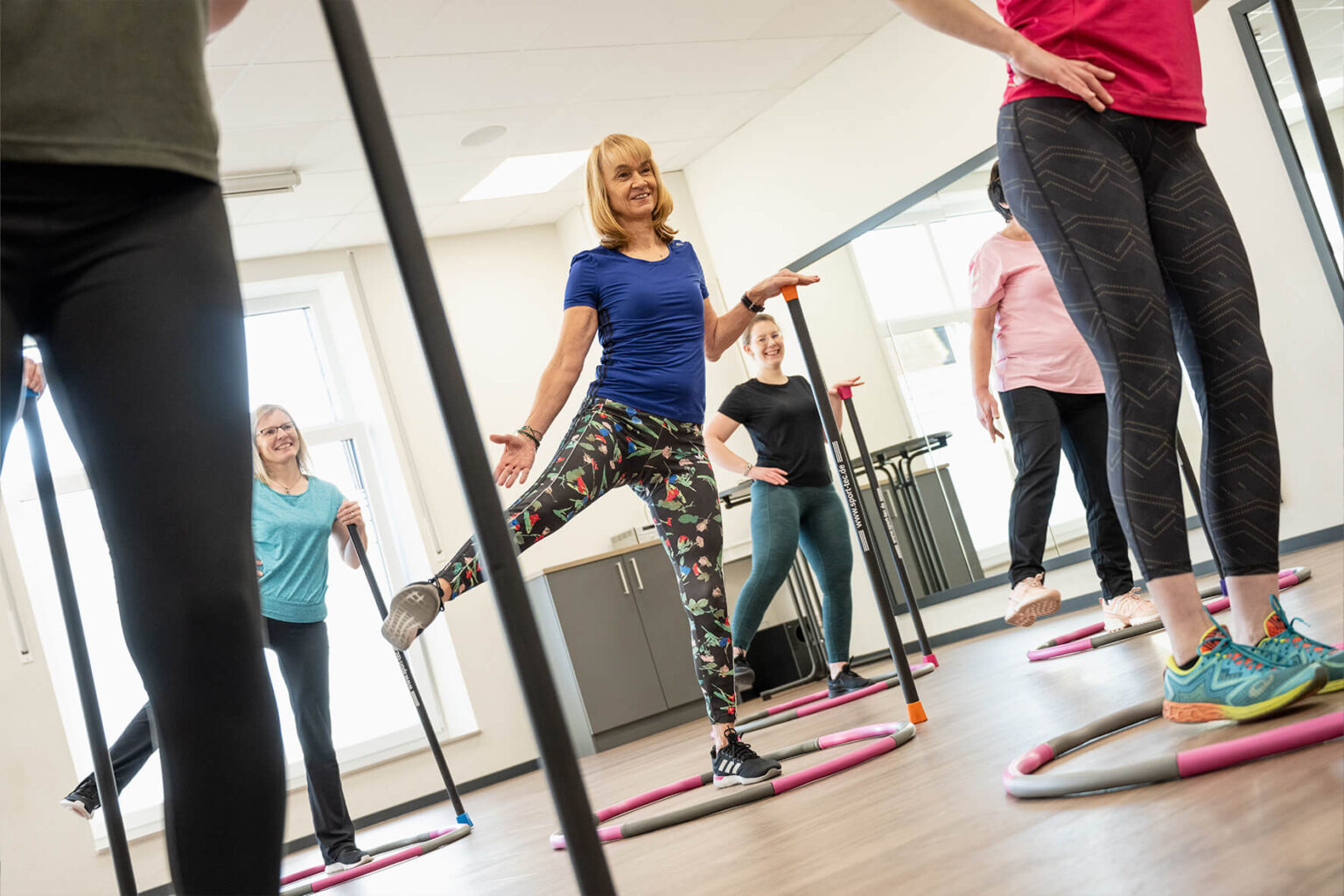 Teilnehmer eines Kurses vom Sport & Therapiezentrum Schumann stützen sich auf einem Stab und heben ein Bein seitlich in die Höhe