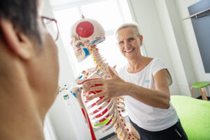 Frau Schumann erklärt den menschlichen Körper anhand eines Skeletts in einem Behandlungsraum vom Sport & Therapiezentrum Schumann